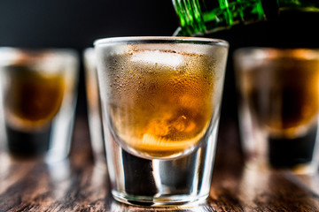 Pouring Whiskey Shots with ice on dark wooden surface.
