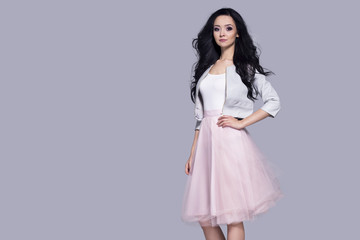 Beautiful young woman in pink skirt standing on a gray background