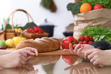 Two women discussing a new menu in the kitchen, close up. Human hands of two persons gesticulating at the table among fresh vegetables. Cooking and friendship concept.