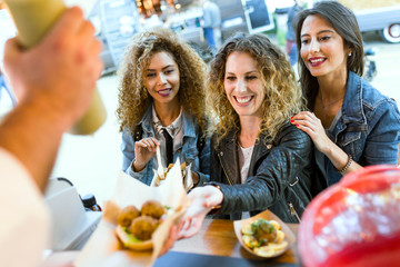 Three beautiful young women visiting eat market in the street.