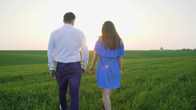 Back look of couple in love walking on the spring wheat field to sky horizon