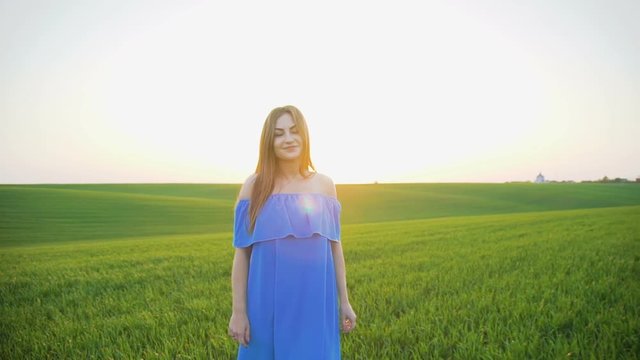 Pretty girl walks to camera on spring green wheat field on the sunset