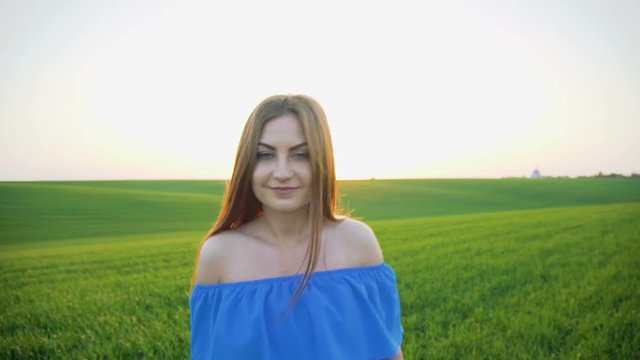 Pretty girl walks to camera on spring green wheat field on the sunset