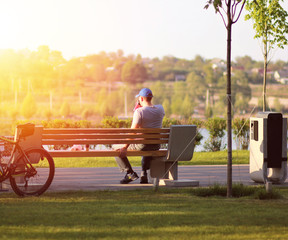 Lonely young man sitting on a bench in the park near the lake on sunset, coffee break