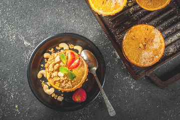 Ideas for a healthy dietary vegan breakfast. Paleo diet. Grilled oranges grapefruits with brown cane sugar, granola, honey, strawberry slices, cashew nuts and mint. On a black stone table. Copy space