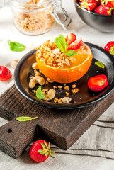 Ideas for healthy vegan breakfast. Paleo diet. Grilled oranges grapefruits with brown cane sugar, granola, honey, strawberry slices, cashew nuts and mint. On a white stone table copy space 