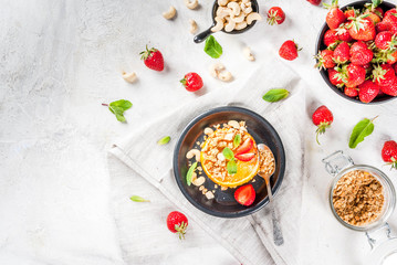 Ideas for healthy vegan breakfast. Paleo diet. Grilled oranges grapefruits with brown cane sugar, granola, honey, strawberry slices, cashew nuts and mint. On a white stone table copy space 