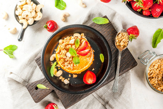 Ideas for healthy vegan breakfast. Paleo diet. Grilled oranges grapefruits with brown cane sugar, granola, honey, strawberry slices, cashew nuts and mint. On a white stone table copy space 