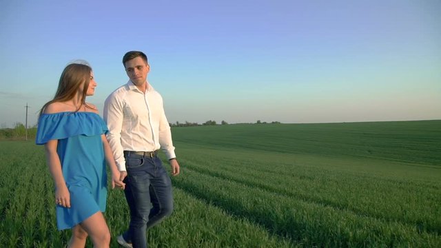 Couple in love walking on the spring wheat field and holds hands on sunset