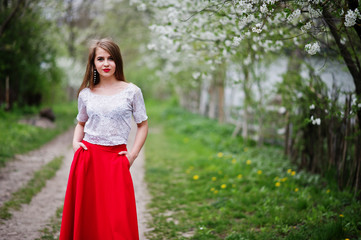 Portrait of beautiful girl with red lips at spring blossom garden, wear on red dress and white blouse.