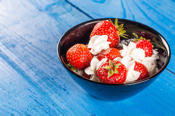 Fresh strawberries in whipped white cream above blue wooden planks background