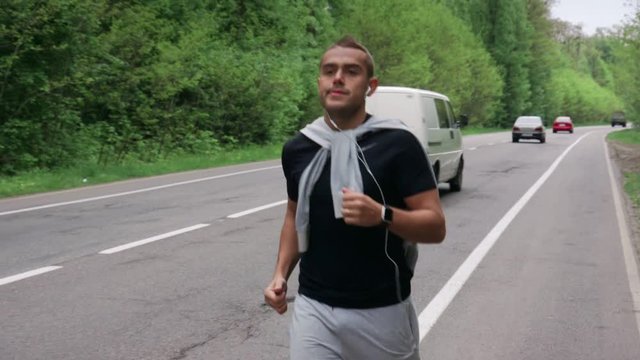 Back look of a young man in hood running on the road near the forest 4K