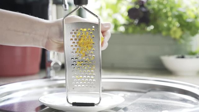 Close up of woman s hand rubbing a lemon peel on a grater in a kitchen. Locked down real time close up shot