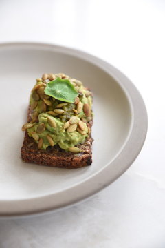 Bread with avocado topping on white plate, close-up