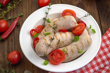 Boiled grilled sausages with cherry tomatoes and chili peppers with greens. Wooden background. Top view. Close-up