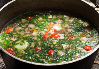 Freshly cooked hot soup in sooty cauldron on camp fire