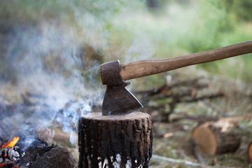 Axe in tree stump and campfire with smoke
