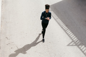 Young woman in sportswear walking on street and looking on her activity tracker