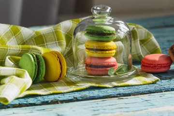 Green, pink and yellow french macarons under the glass on the wooden boards