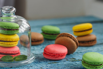 Green, pink and yellow french macarons under the glass on the wooden boards