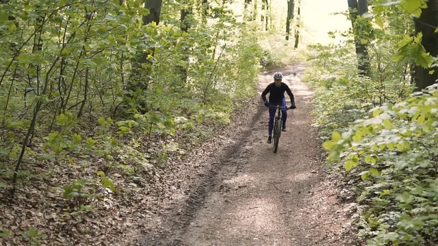 Young sports man riding bicycle on the tree forest road, sunny spring day, 120FPS slowmotion