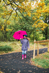 Young cheerful stylish woman walks the road in park with pink umbrella