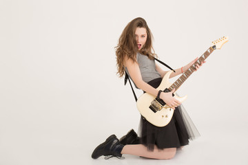 Fototapeta premium Hot girl emotionally playing the electric guitar standing on her knees isolated. Brunette model playing hard rock music and singing at camera isolated. Sexy musician girl with dark lipstick