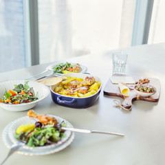 Plate of roasted chicken with potato served with green salad on table in modern apartment in front of window