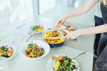 Roasted chicken with potato, green salads on table against window in modern apartment