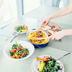 Close-up of woman preparing dinner with roasted chicken with potato serving with green salads on table in modern apartment