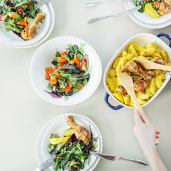 Top view on table with tasty roasted chiсken, potato, healthy salad. Female hands holding wooden spoon