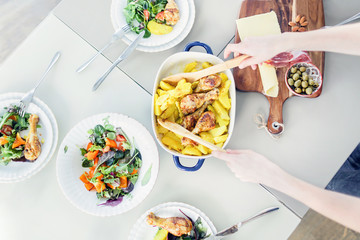 Woman preparing chicken with potato dish, plates of vegetable salad on table. Top view