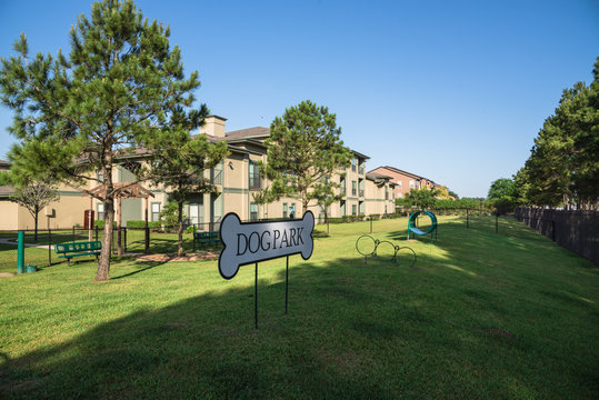 Community on-site dog park at the grassy backyard of a typical apartment complex building in suburban area at Humble, Texas, US. Off-leash dog park with pet stations, toys and bag dispensers