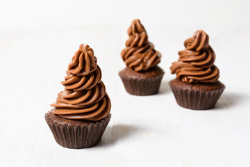 Three chocolate cupcakes on white wooden table