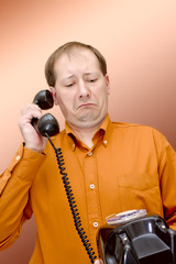 A white man in an orange shirt and glasses with a telephone receiver in the rivers looks at the old disk-type wired telephone with surprise and bewilderment