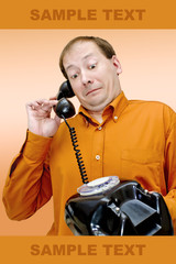 A white man in an orange shirt and glasses with a telephone receiver in the rivers looks at the old disk-type wired telephone with surprise and bewilderment