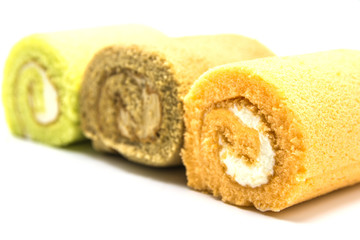 A close-up of three colorful Swiss roll cakes in yellow, brown, and green, highlighting the soft texture and creamy filling.