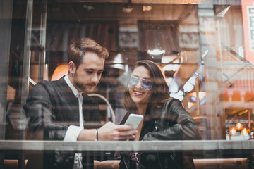 Friends using mobile in a cafe. Couple of lovers having a good time with the cell phone.