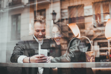 Friends using mobile in a cafe. Couple of lovers having a good time with the cell phone.