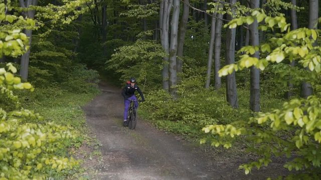 Young backpacked sports man riding bicycle on the tree forest road, spring sundown, 120FPS slowmotion