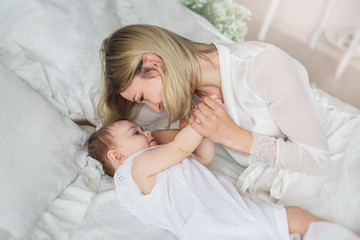 Happy young mother plays with her little baby on a bed