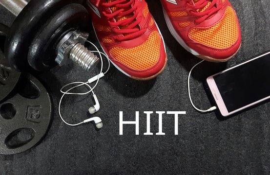 Dumbbell, smartphone and sport shoes on gym floor with word HIIT 