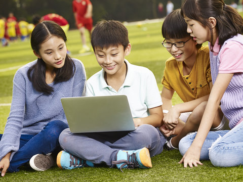 asian elementary school children using laptop outdoors
