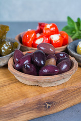 Mediterranean appetizer antipasti tapas bowls with green and calamata olives, feta cheese, stuffed pepper, herbs on wooden plank