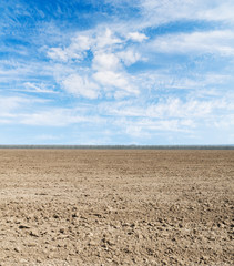 black plowed field and blue sky with clouds