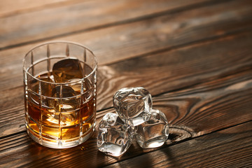 Glass of whiskey with ice cubes on wooden table