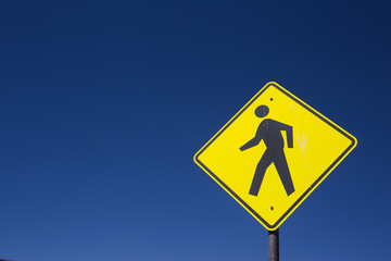 Yellow pedestrian caution sign at crossing way and intersection with blue sky background for safety transportation and people in the city