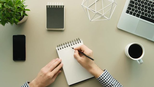 Man writing ideas on daily notebook on grey office table background. Top view. Shot from above