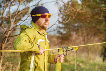 Fototapeta premium Close-up portrait of a man adjusting slacklining equipment before performing crazy slacklining tricks and walking on slacklin in a park in nature