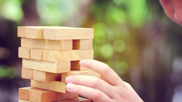 Slow motion of little kid hand play with wood block to build tower in the garden.